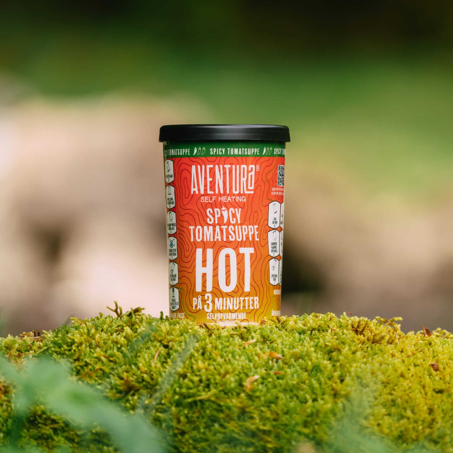 
                  
                    Aventura Self Heating Spicy Tomato Soup in 3 minutes on a log in the forest with moss below it.
                  
                
